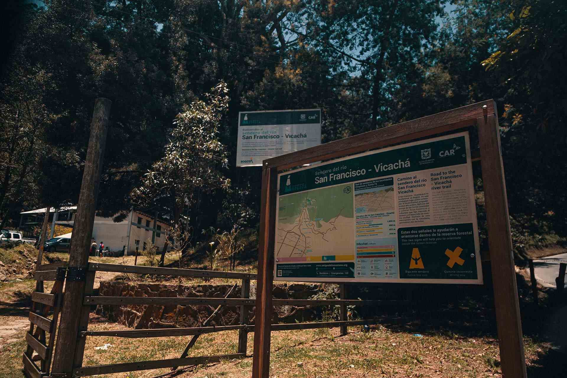  Sendero San Francisco - Vicachá letrero en madera de ingreso rodeado de frondosos árboles y una casa blanca al fondo. 