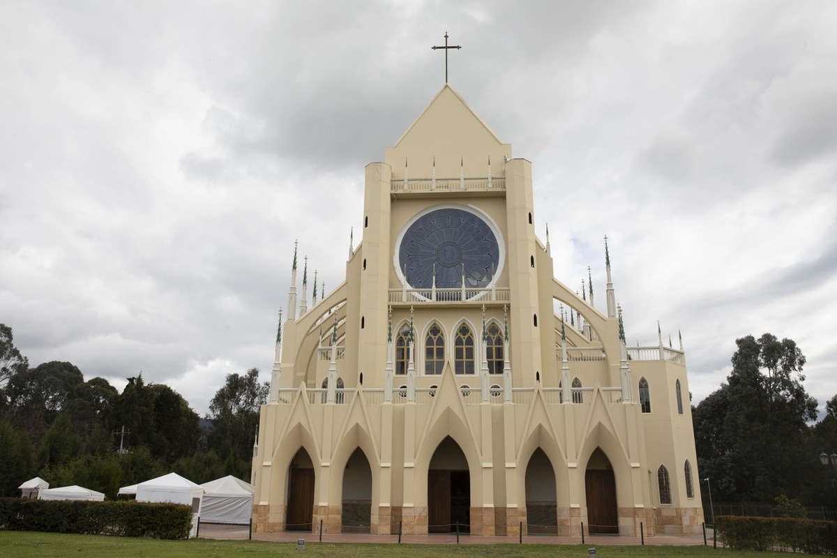  Iglesia Caballeros de la virgen nuestra Señora de Fátima, fachada completa de frente rodeada de árboles y cielo gris con nubes blancas
