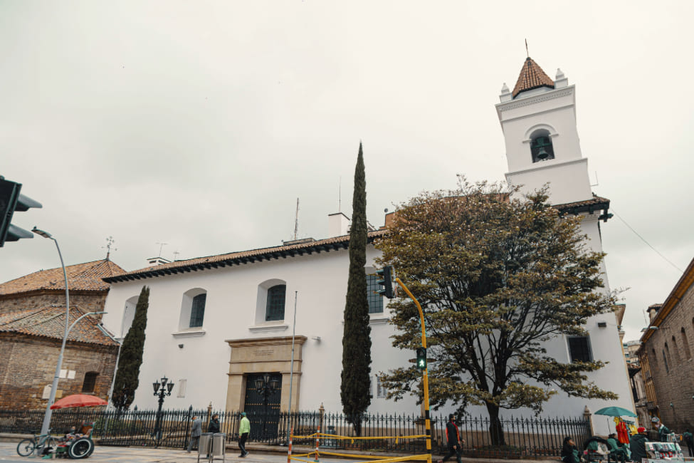 Parroquia de La Veracruz fachada blanca vista lateral rodeada de árboles y algunos vendedores ambulantes en bicicleta.