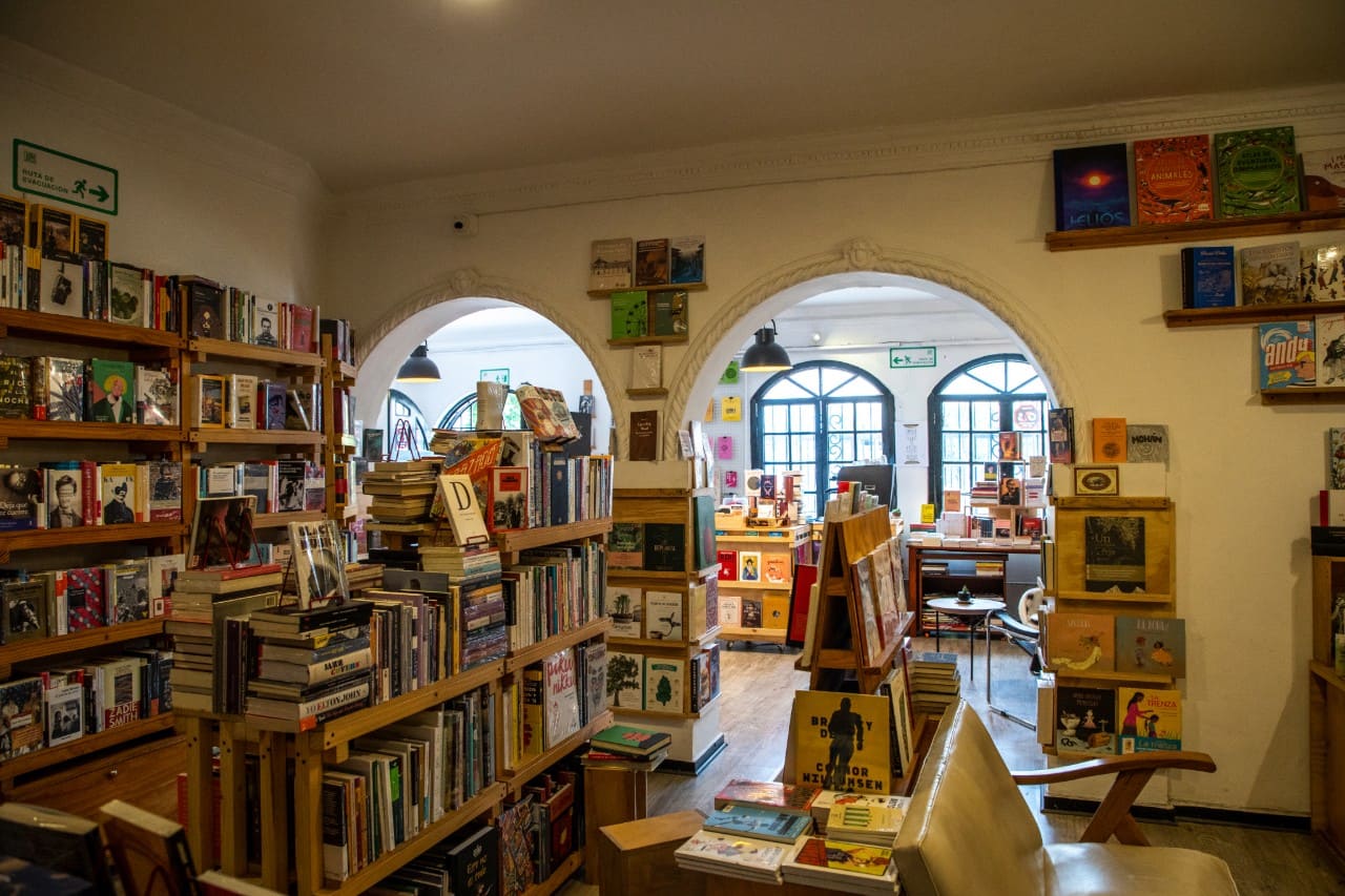 Librería Garabato, sala abarrotada con libros en estanterías en pared y piso. Dos arcos en la pared conducen a otra sala donde se ven más libros y unas ventanas al exterior donde hay luz de día.