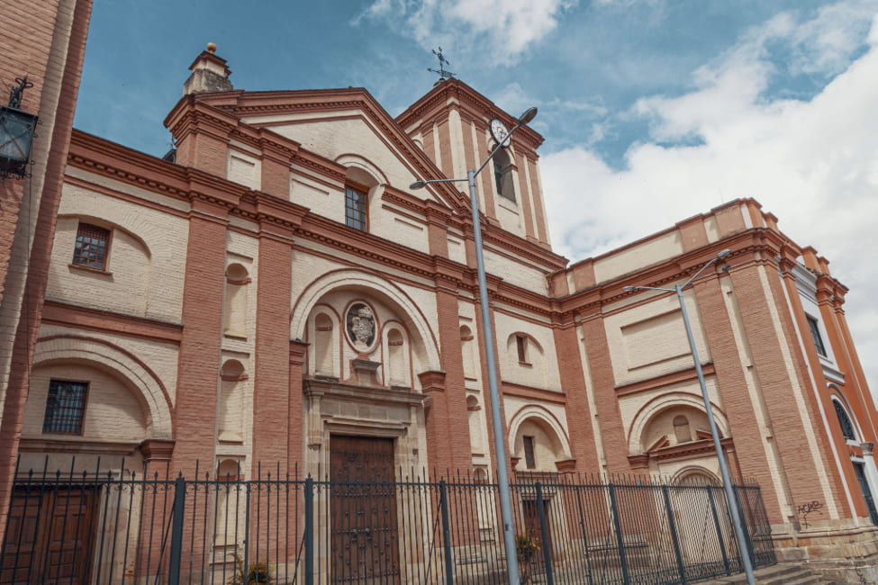  Iglesia San Ignacio Loyola fachada completa en la drillo y pintura amarilla en la que se ven ocho ventanas y cuatro puertas. En la torre más alta se observa el reloj.