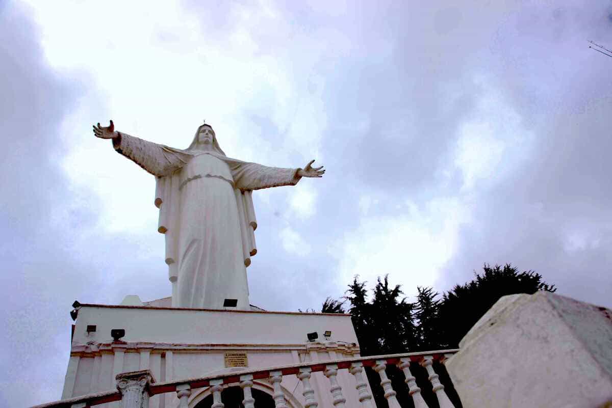 Sendero Guadalupe - Aguanoso con imágen de la Virgen de Guadalupe y sus brazos abiertos en contrapicado con cielo gris.