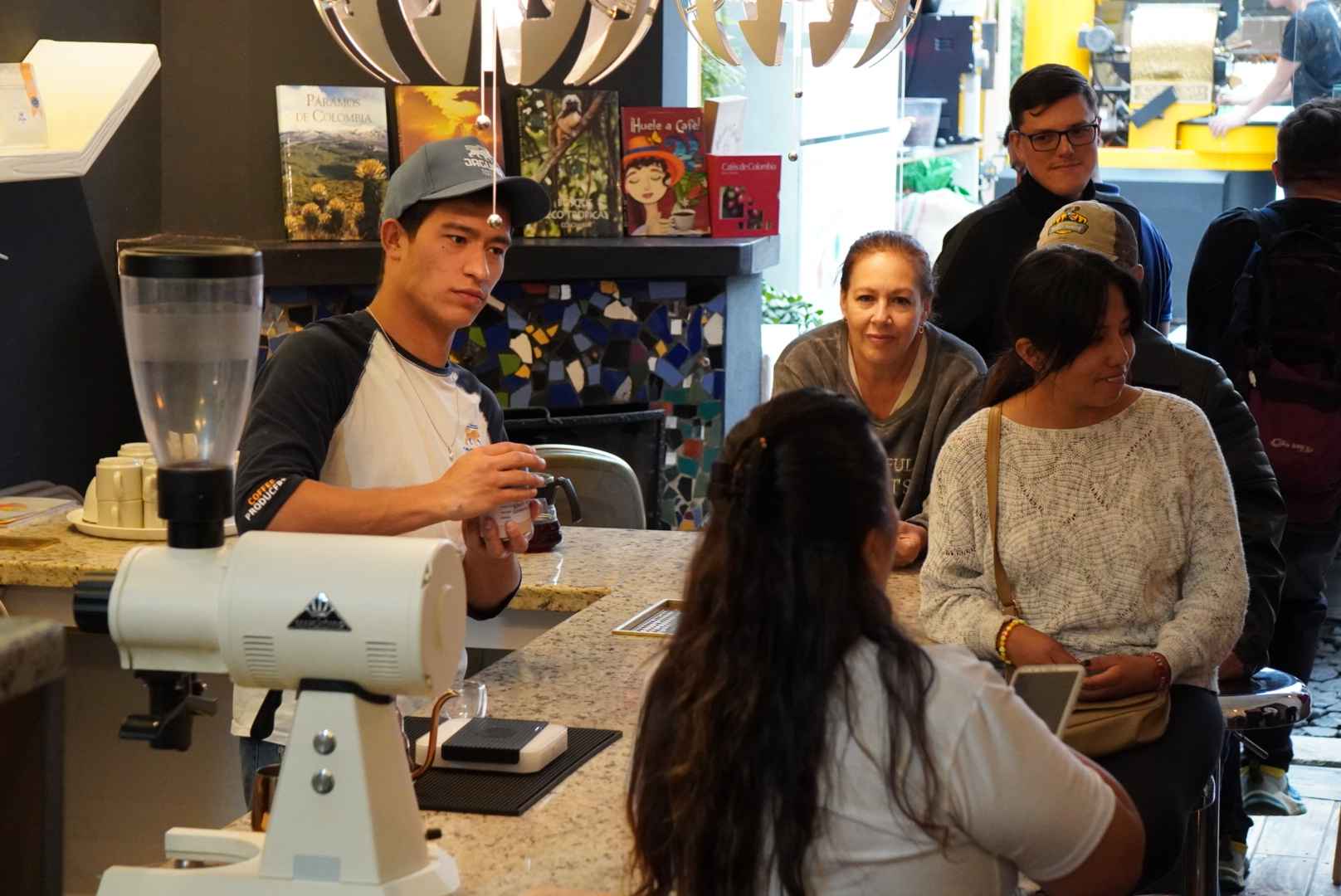Grupo de personas jóvenes observan a un joven que prepara café. hay una máquina de preparar café sobre una mesa.