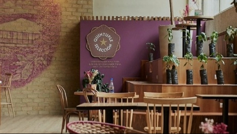 Salón interior de un restaurante rodeado de plantas pequeñas, mesas y silas de madera.