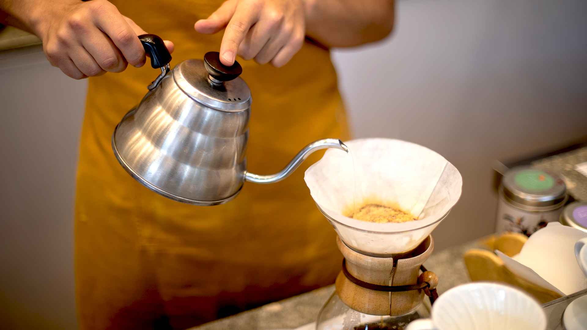 Barista prepara café con método pour-over, vertiendo agua en un cono que filtra el café hacia una jarra de vidrio.