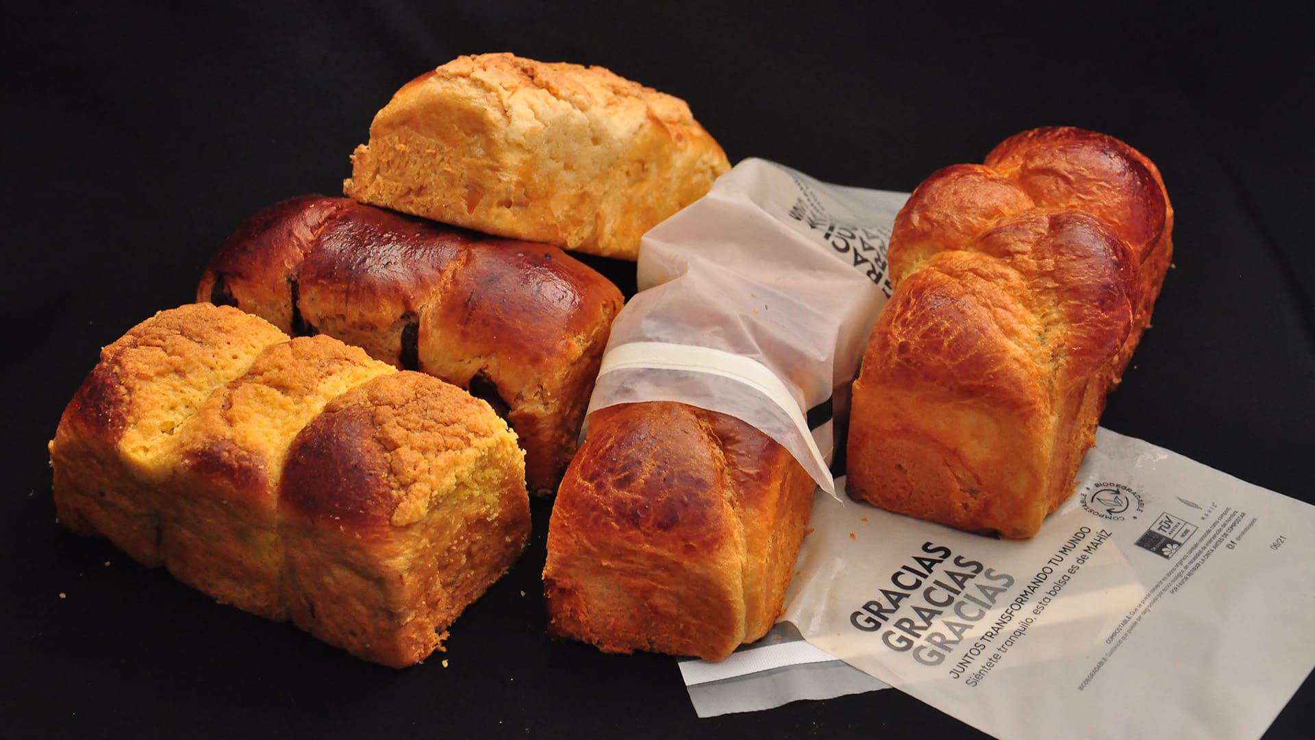 Varios panes dulces, algunos envueltos en papel con la palabra "GRACIAS", sobre un fondo negro.