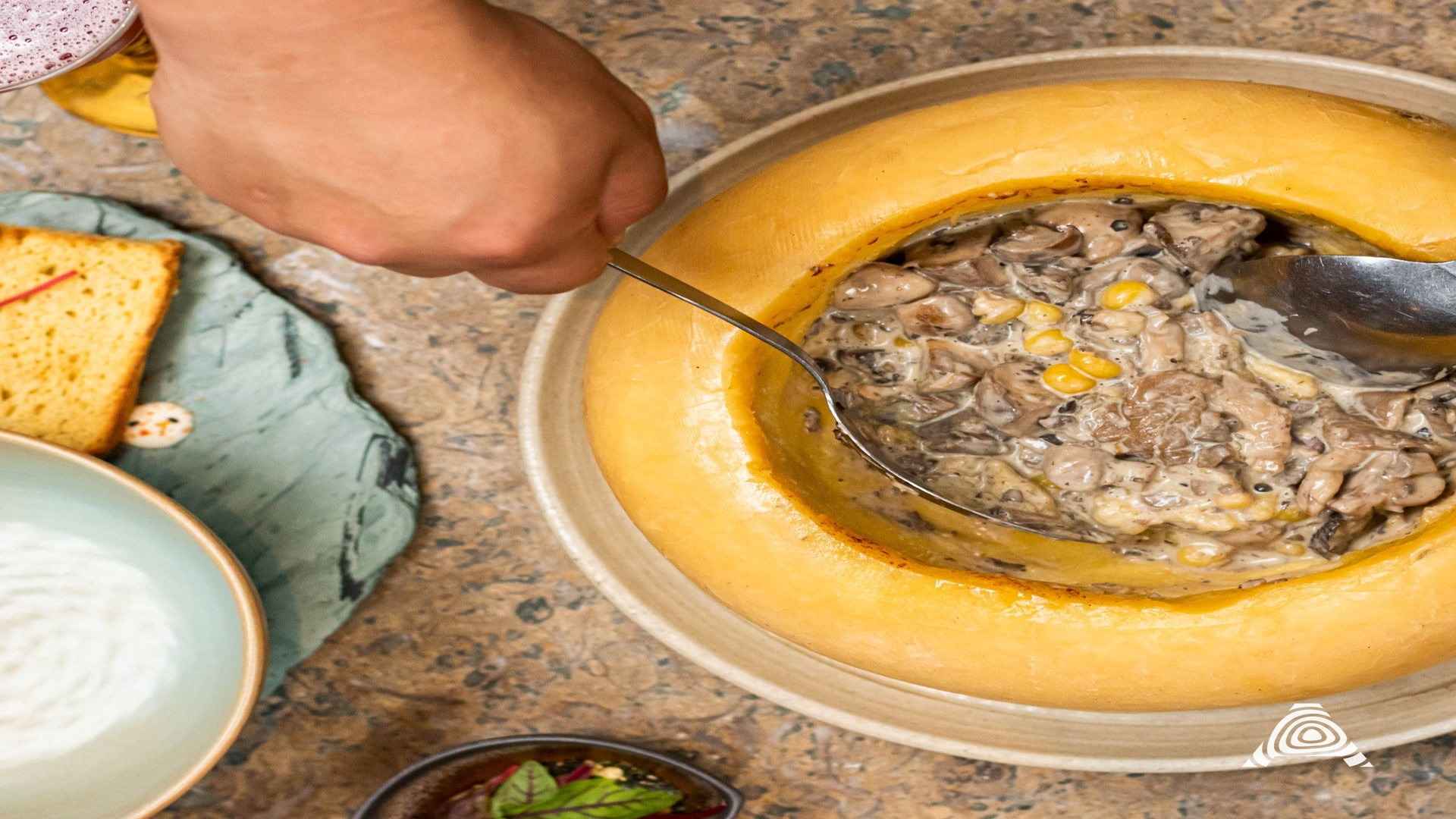 Un plato cremoso de champiñones con maíz, servido dentro de una hogaza de pan, siendo disfrutado en una mesa rústica.