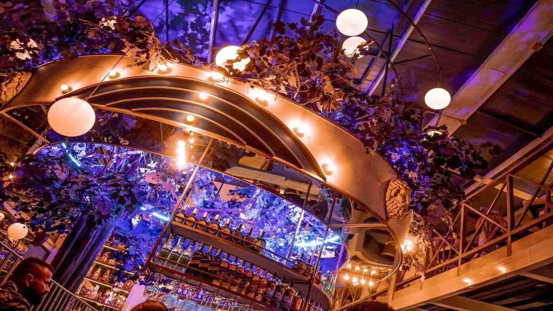 Un bar con un diseño interior extravagante, con iluminación púrpura, follaje y botellas de licor.
