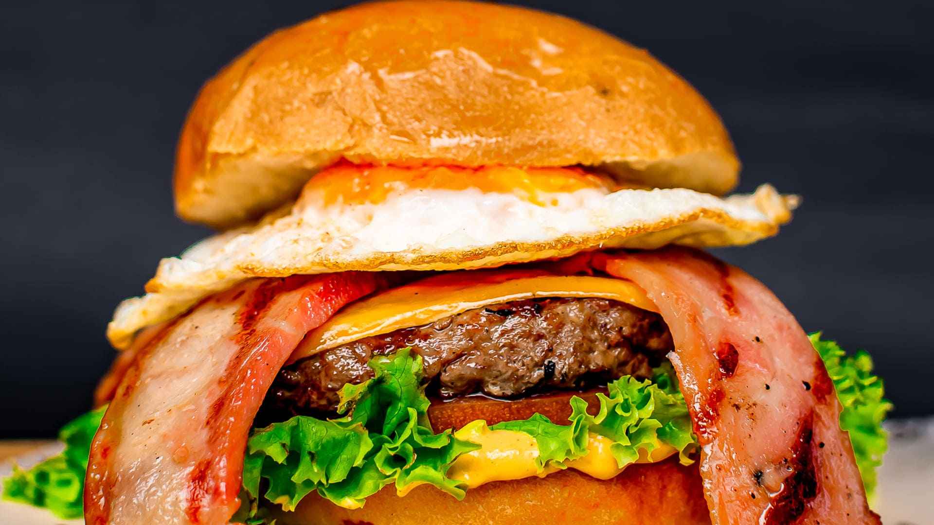 Un apetitoso primer plano de una hamburguesa con carne, queso, lechuga, tomate, tocineta y huevo frito.