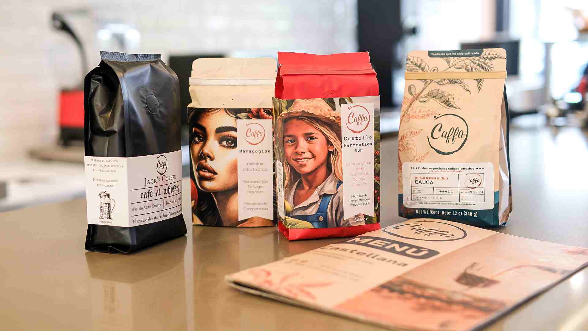 Varios paquetes de café "Caffa" con diseños artísticos y un menú, exhibidos sobre una superficie.