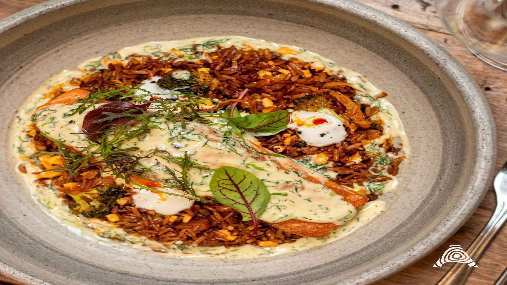 Un filete de salmón perfectamente cocido, cubierto con una salsa de eneldo, sobre una cama de arroz integral y brócoli.