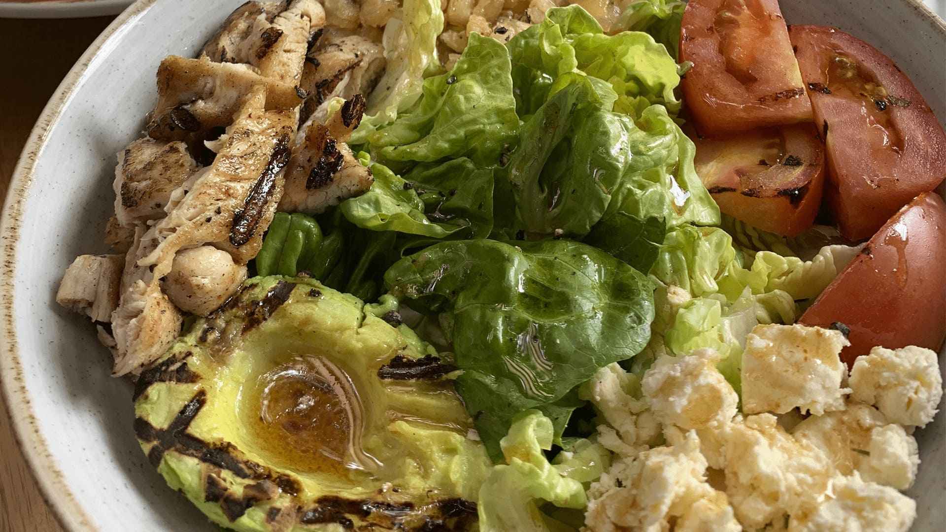 Ensalada fresca con pollo a la parrilla, aguacate, tomate, lechuga y queso feta, aderezada con vinagreta.