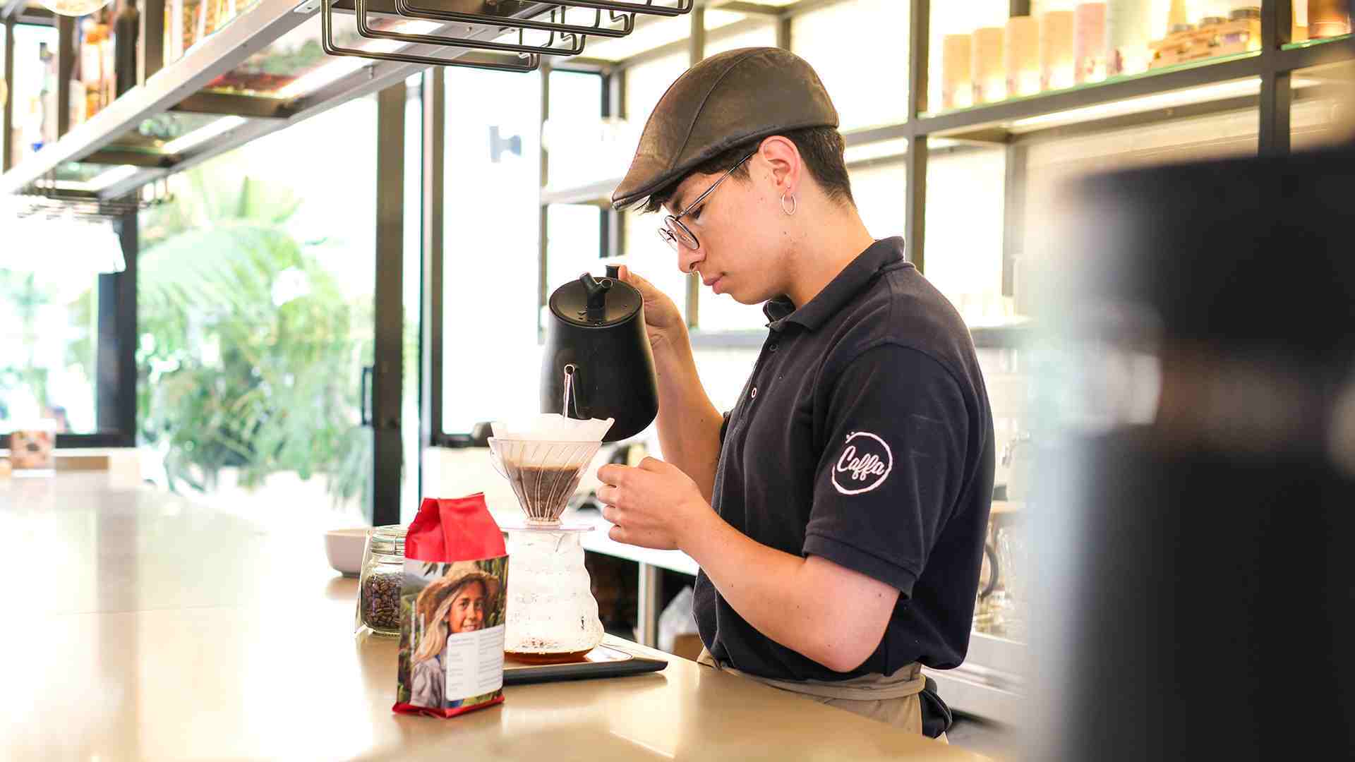 Un barista con gorra y gafas prepara café de goteo en Caffa, concentrado en el proceso.