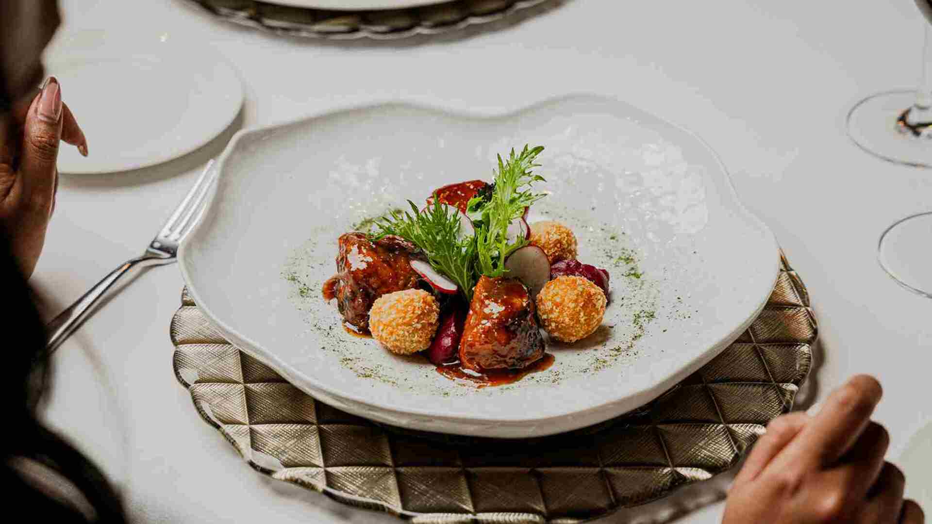 Un plato gourmet exquisitamente presentado con carne, rábanos y esferas crujientes en un restaurante de lujo.