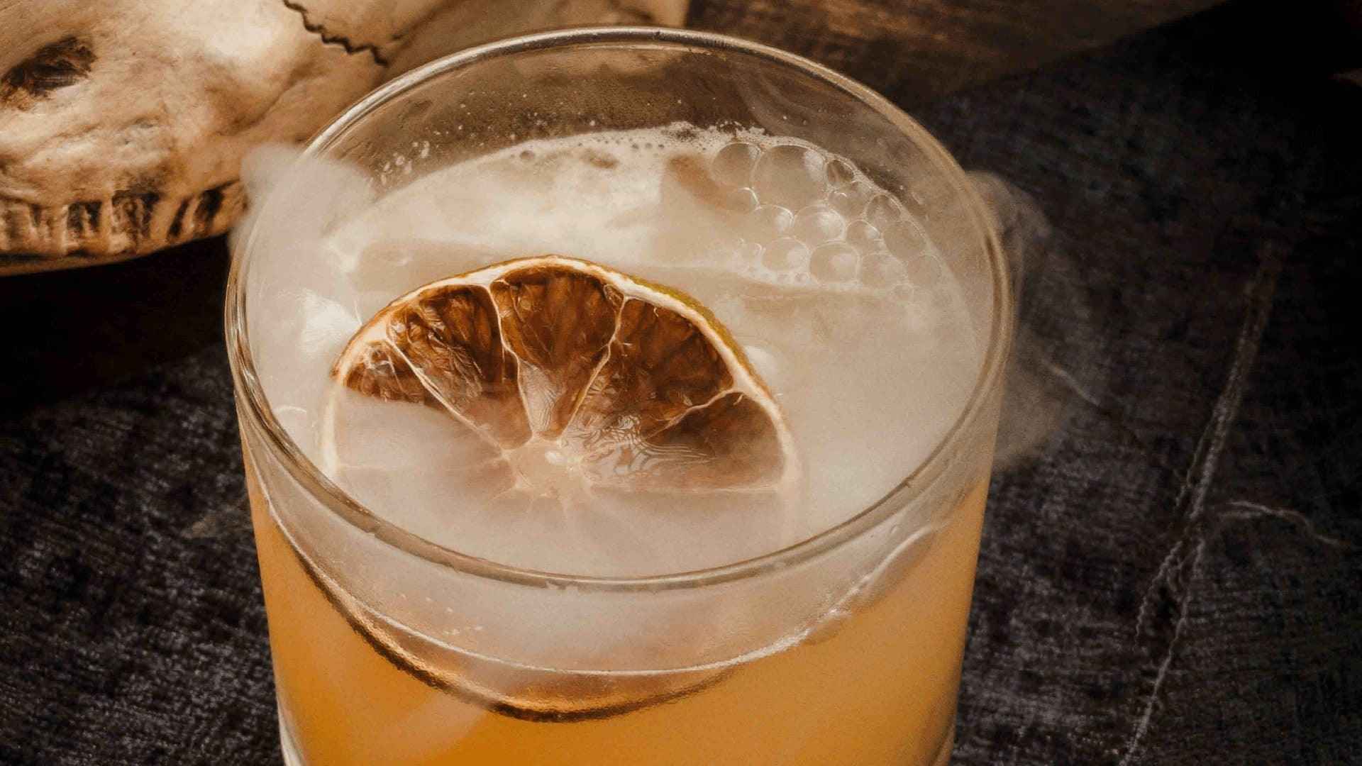  Un cóctel humeante con una rodaja de lima deshidratada en un vaso de cristal.