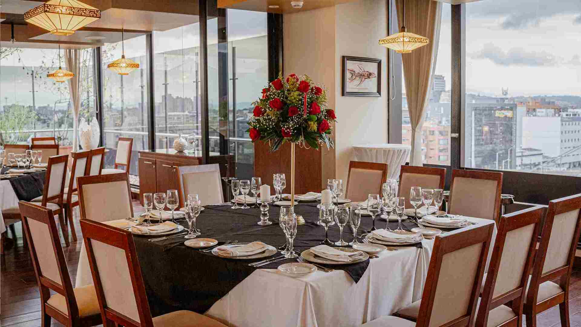 Un elegante comedor de restaurante con mesas puestas para un evento, decorado con un gran arreglo floral y vistas a la ciudad.