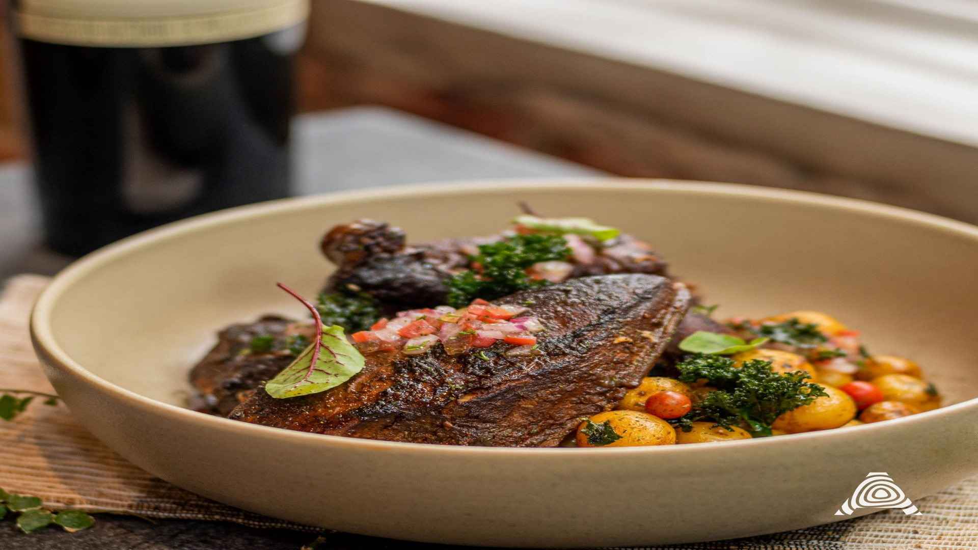 Un plato elegante con un corte de carne oscura, acompañado de papas baby y una fresca ensalada picada, en un ambiente acogedor.