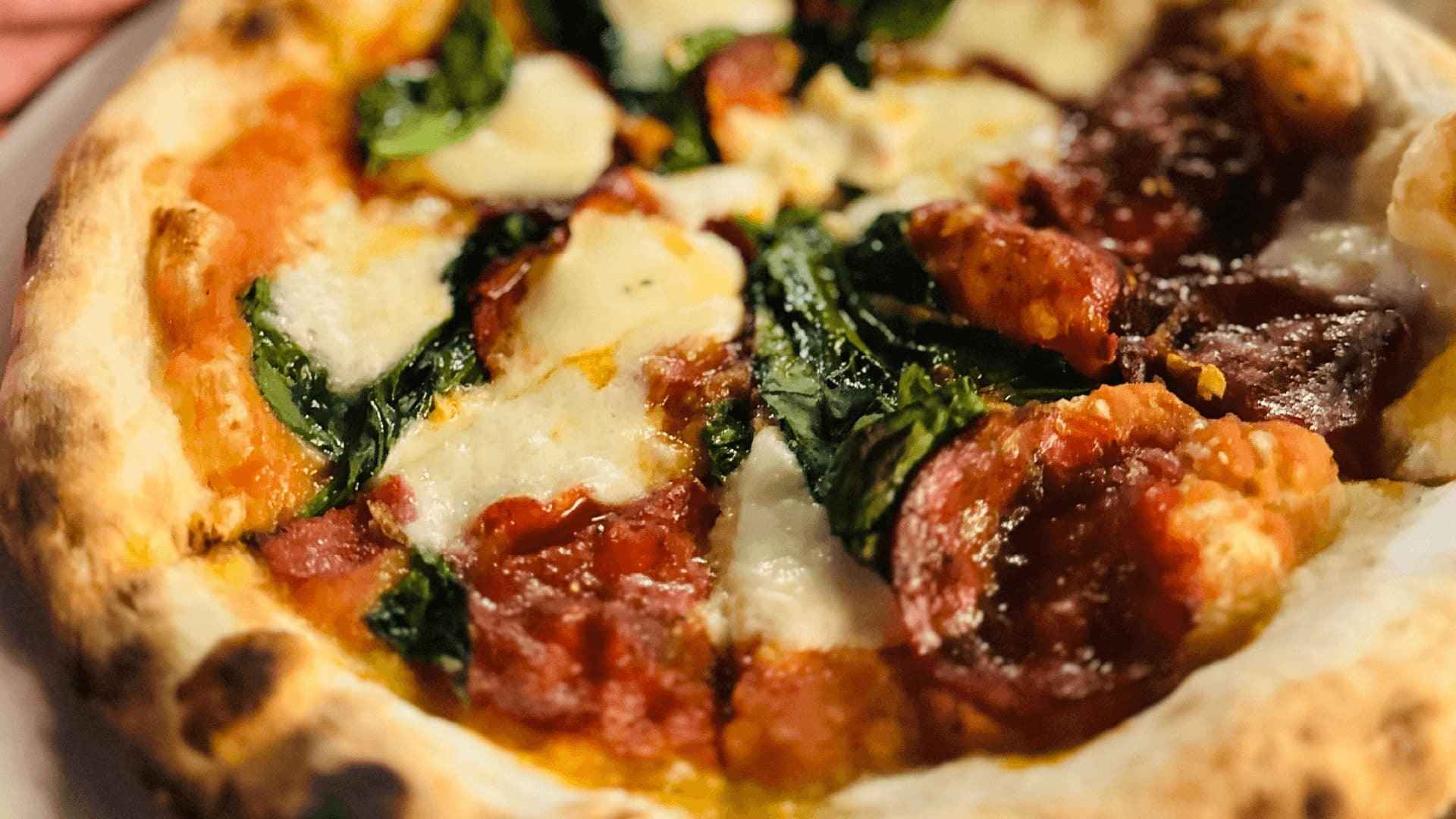 Un primer plano de una pizza artesanal recién horneada con queso derretido, pepperoni y espinacas.