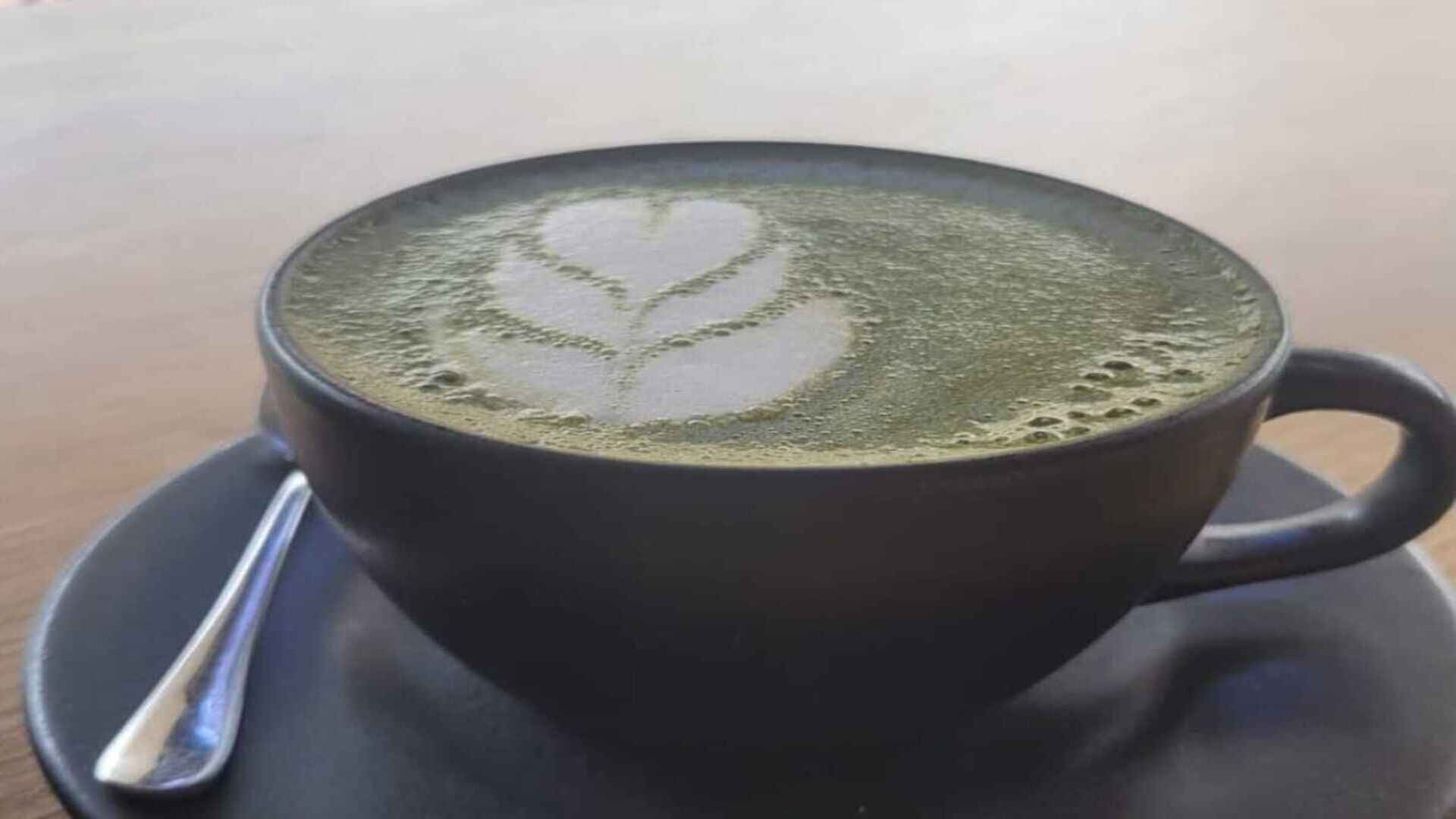  Una taza oscura de matcha latte con arte de espuma en forma de flor, sobre un platillo a juego. Pie de foto: Disfruta de la calma y el sabor único de un matcha latte perfectamente preparado.