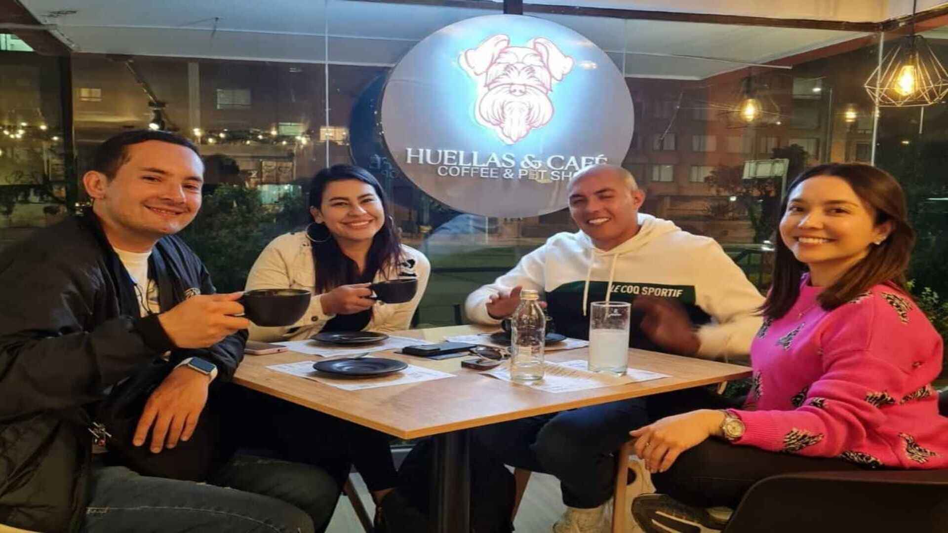 Cuatro amigos sonrientes disfrutando de un café en "Huellas & Café", con un ambiente cálido y acogedor.