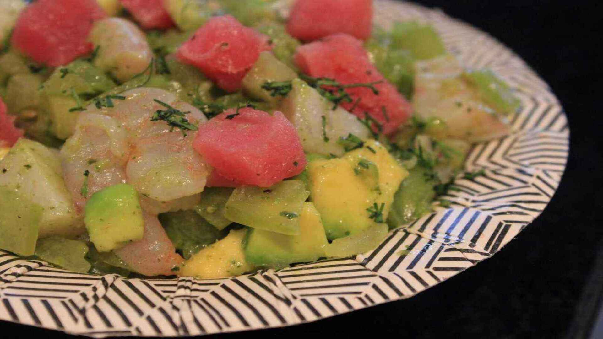 Ceviche fresco con cubos de sandía, aguacate y mango, mezclado con hierbas aromáticas, en un plato único.
