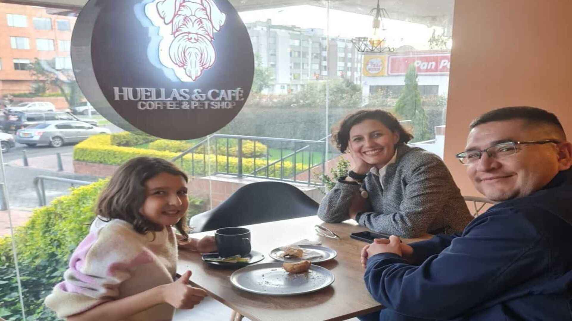 Una familia sonriente disfrutando de un agradable momento en "Huellas & Café", con vista a la calle.