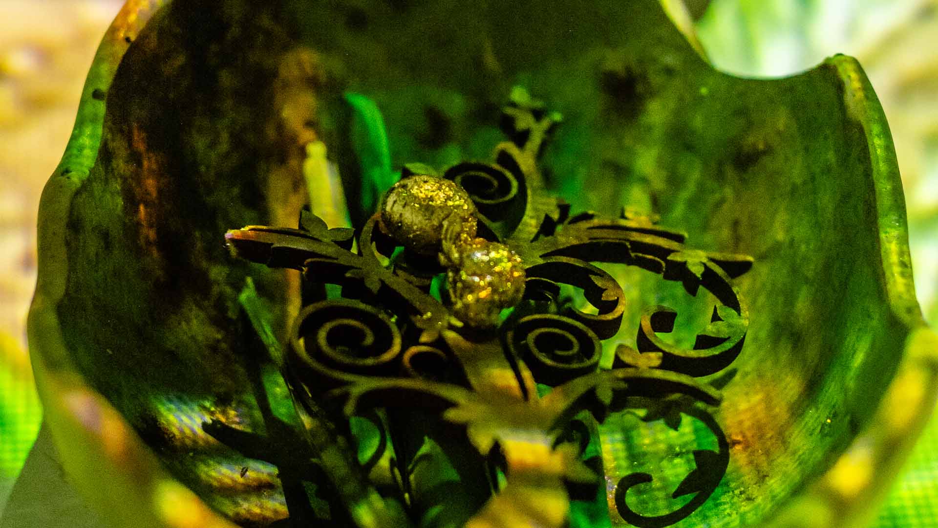 Detalle intrincado de un adorno dorado y oscuro, sumergido en un vibrante entorno verde y brillante.