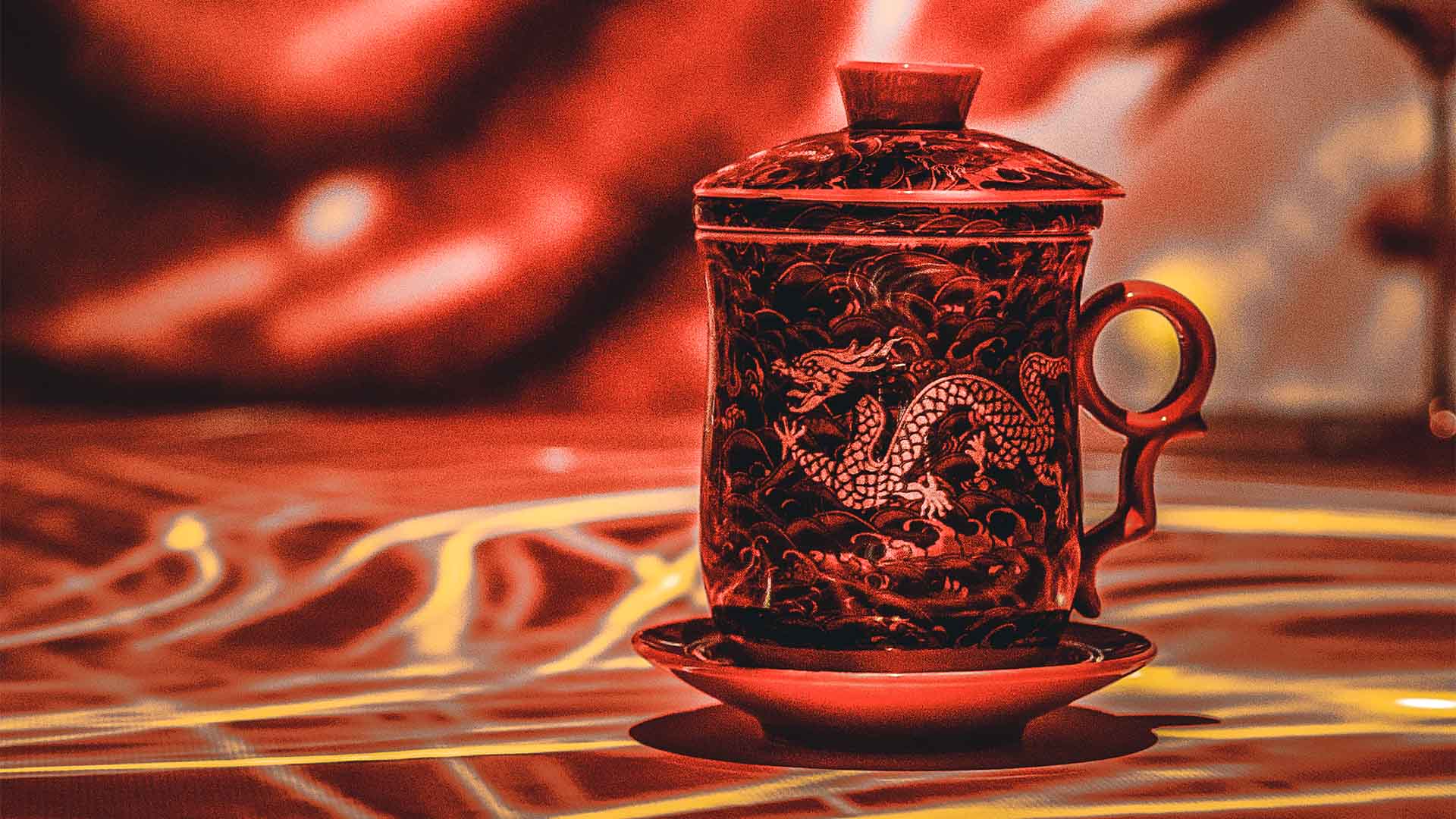 Taza de té con tapa y plato, decorada con un dragón chino, iluminada con tonos rojos y dorados.