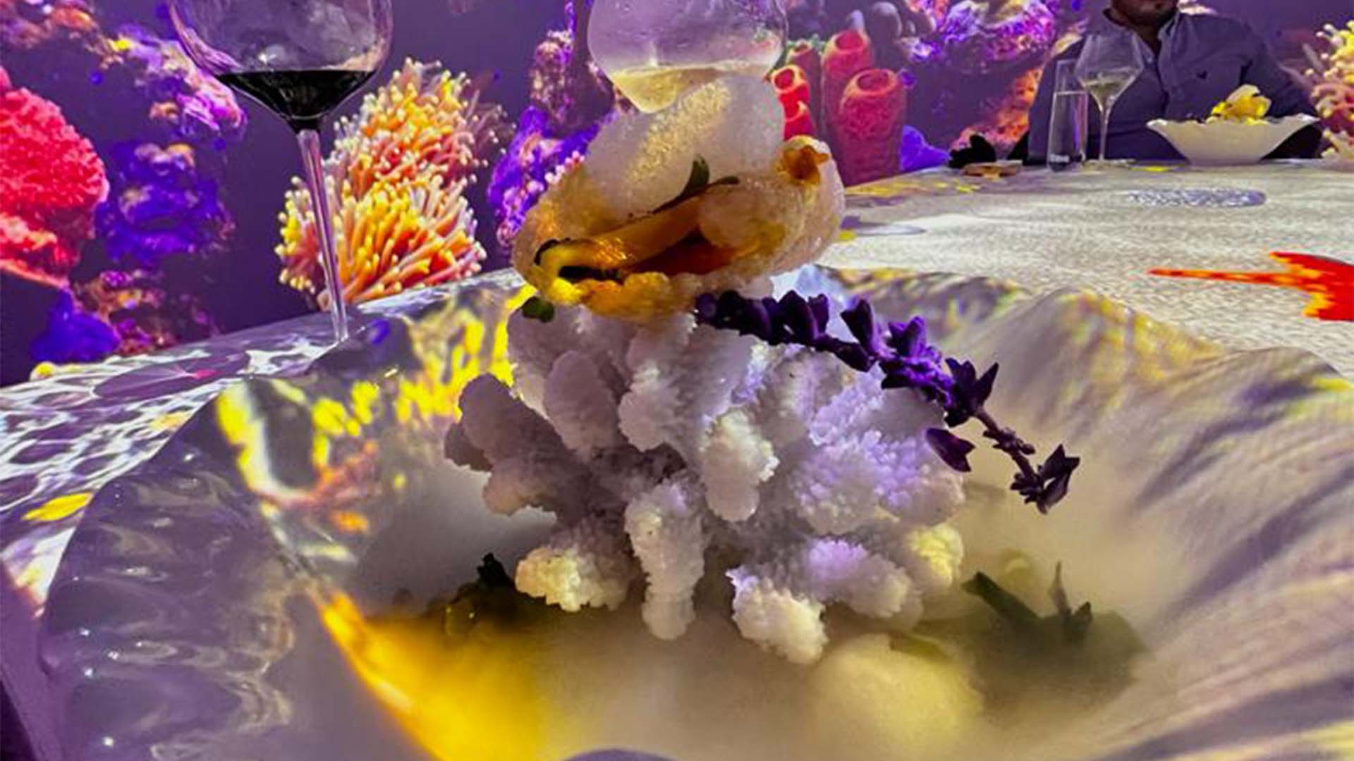 Plato innovador con decoración que simula coral, acompañado de un elemento comestible y flores moradas.