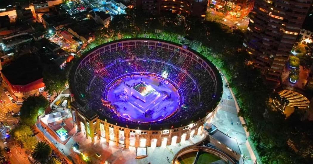 Vista interior desde arriba y de noche de la Plaza La Santamaría, una estructura circular rodeada por árboles y que está iluminada en su centro.