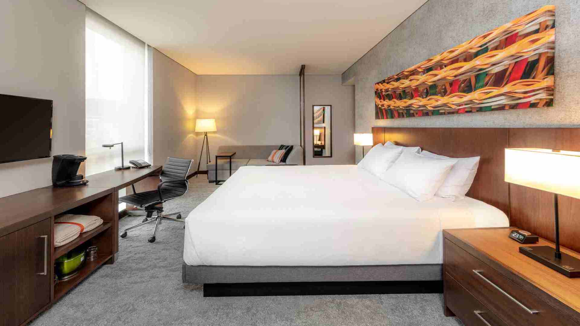  La entrada del hotel Hyatt Place, con una marquesina de cristal, el logo iluminado y un diseño exterior elegante. Los jardines frontales añaden un toque de naturaleza.