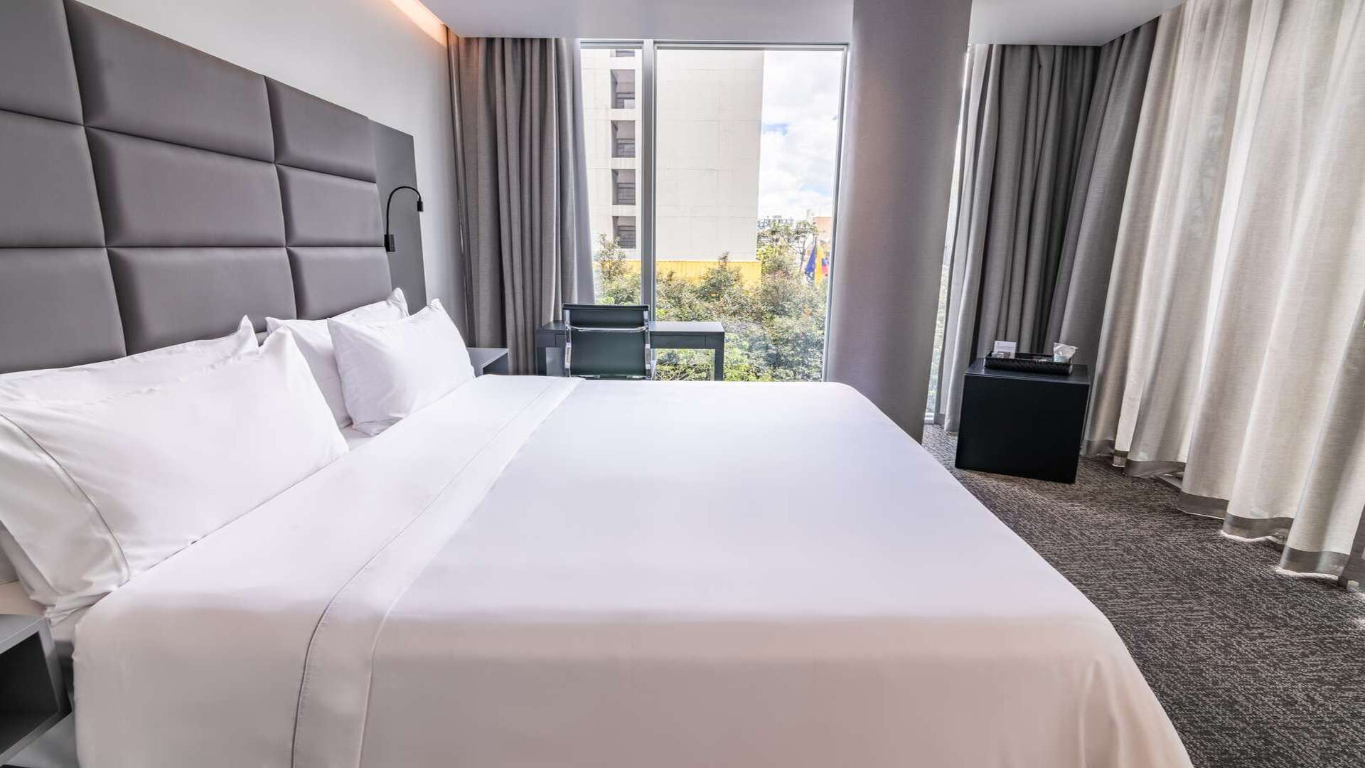 Habitación de hotel con dos camas dobles, cabeceras grises y amplios ventanales.