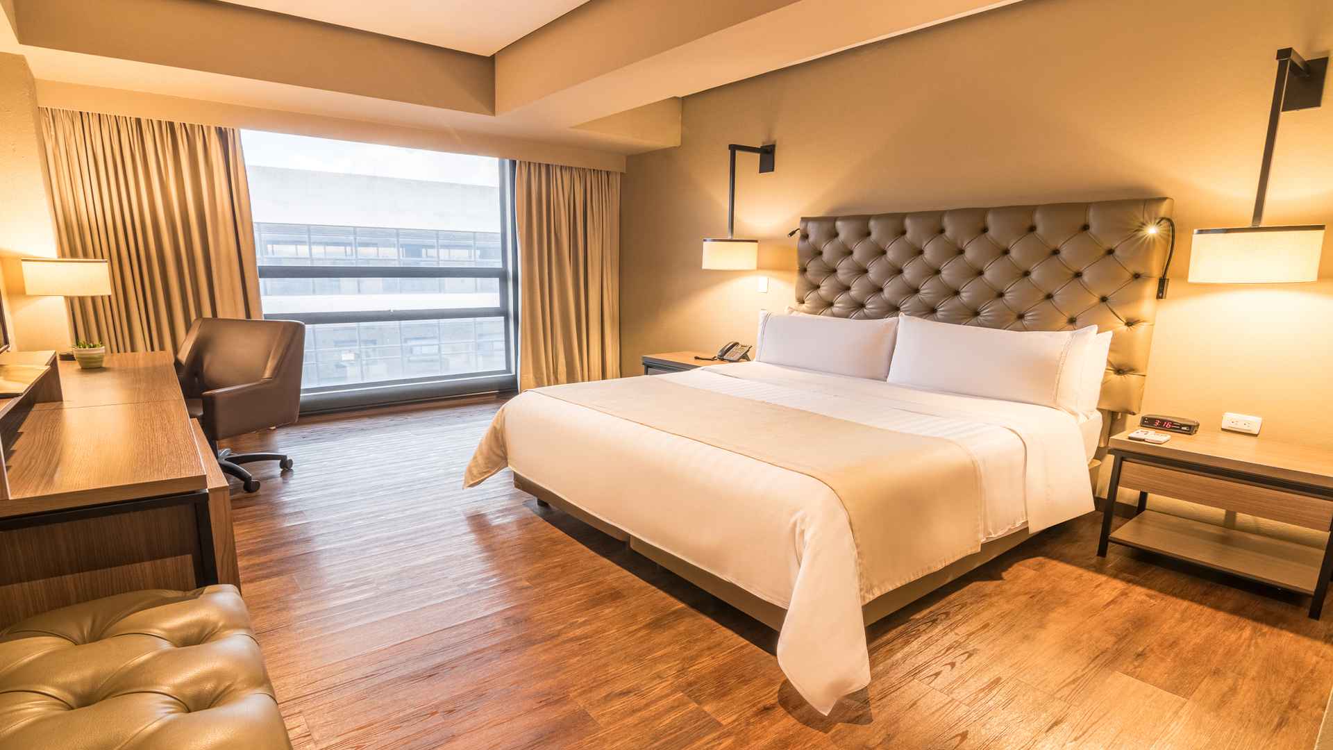Habitación de hotel con cama king-size, cabecera capitoné y escritorio funcional.