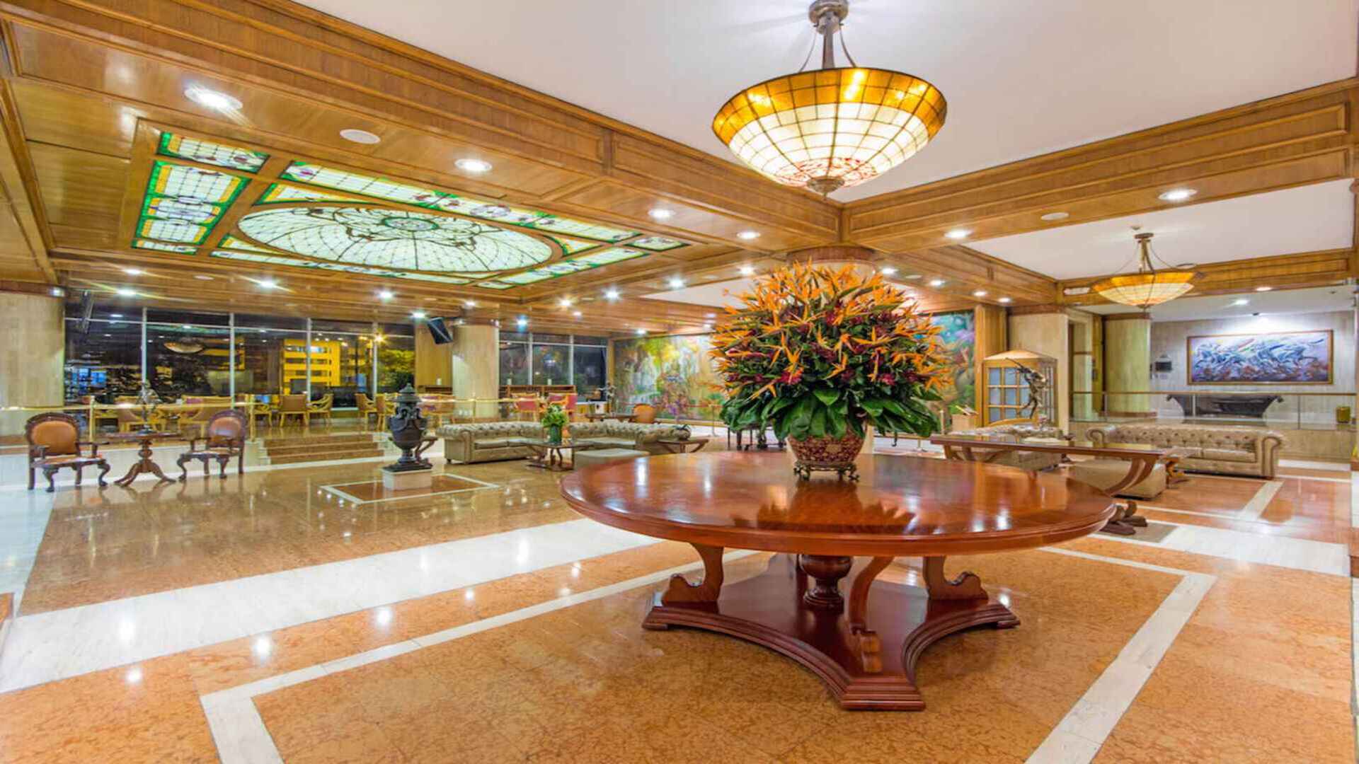  Lujoso lobby de hotel con una gran mesa central y vitrales. Impresionante entrada con decoración floral.