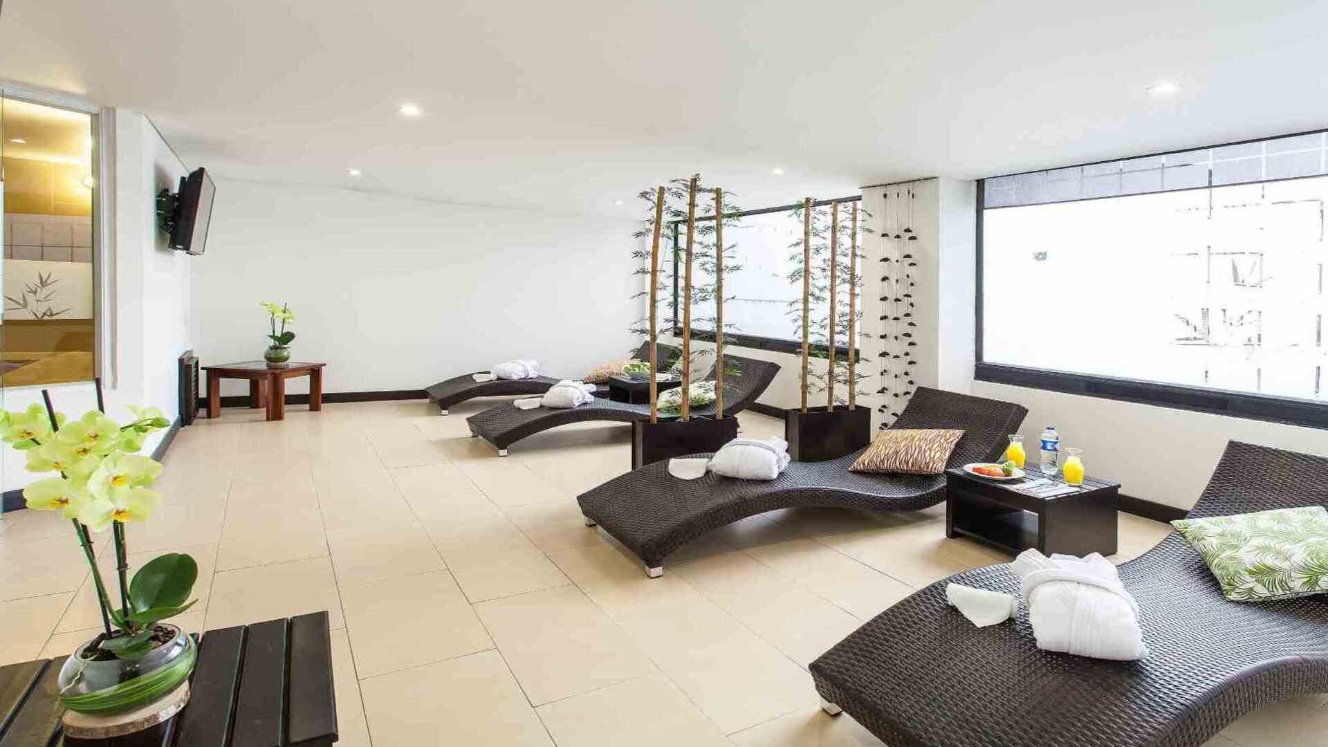Un área de relajación tipo spa con varias tumbonas de mimbre, batas blancas y orquídeas decorativas. El espacio es luminoso y sereno.