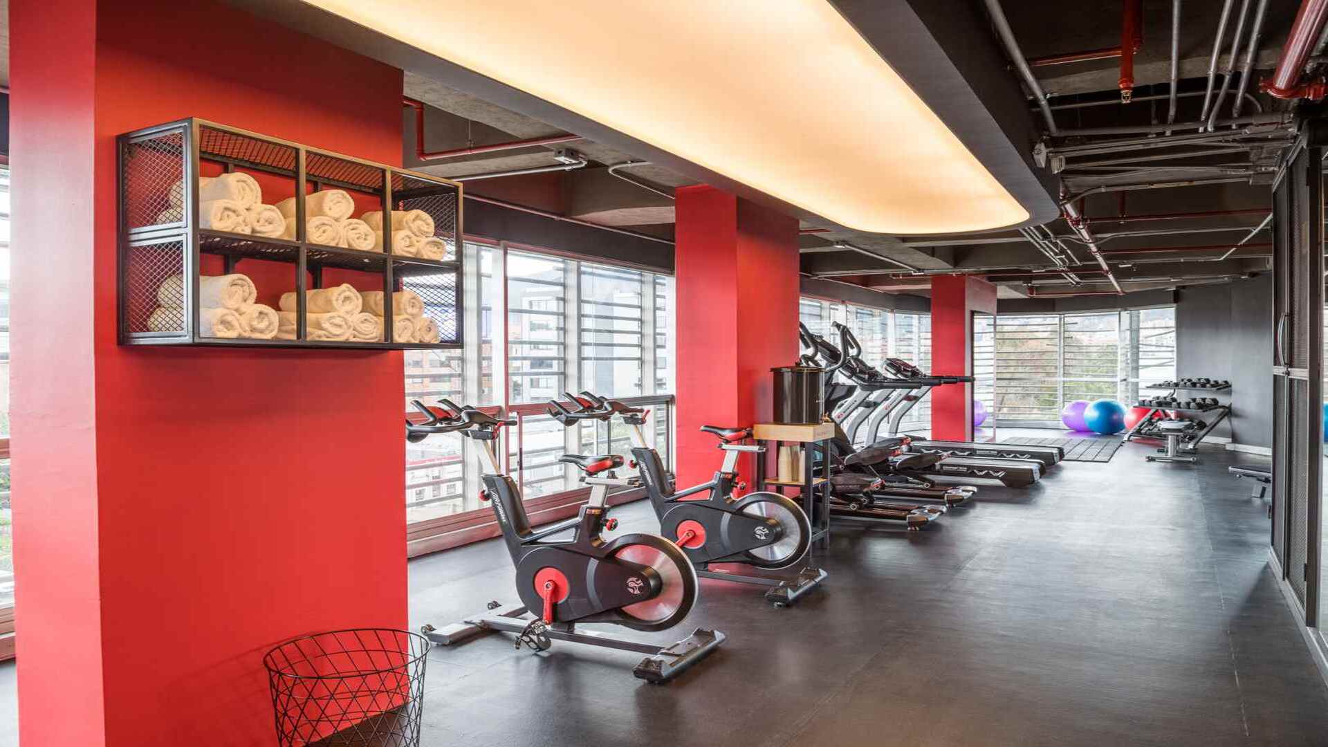 Un gimnasio moderno con paredes rojas, bicicletas estáticas y cintas de correr. Las toallas enrolladas están listas para los usuarios.