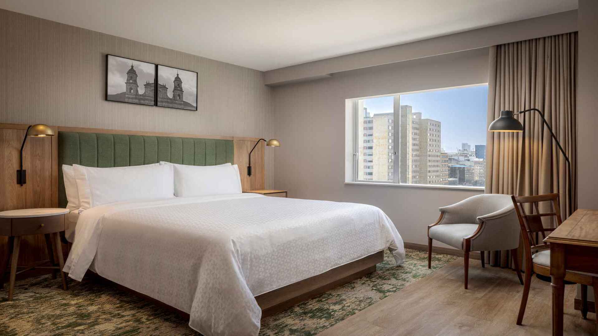 Habitación de hotel con cama king-size, cabecera verde y vista a la ciudad.