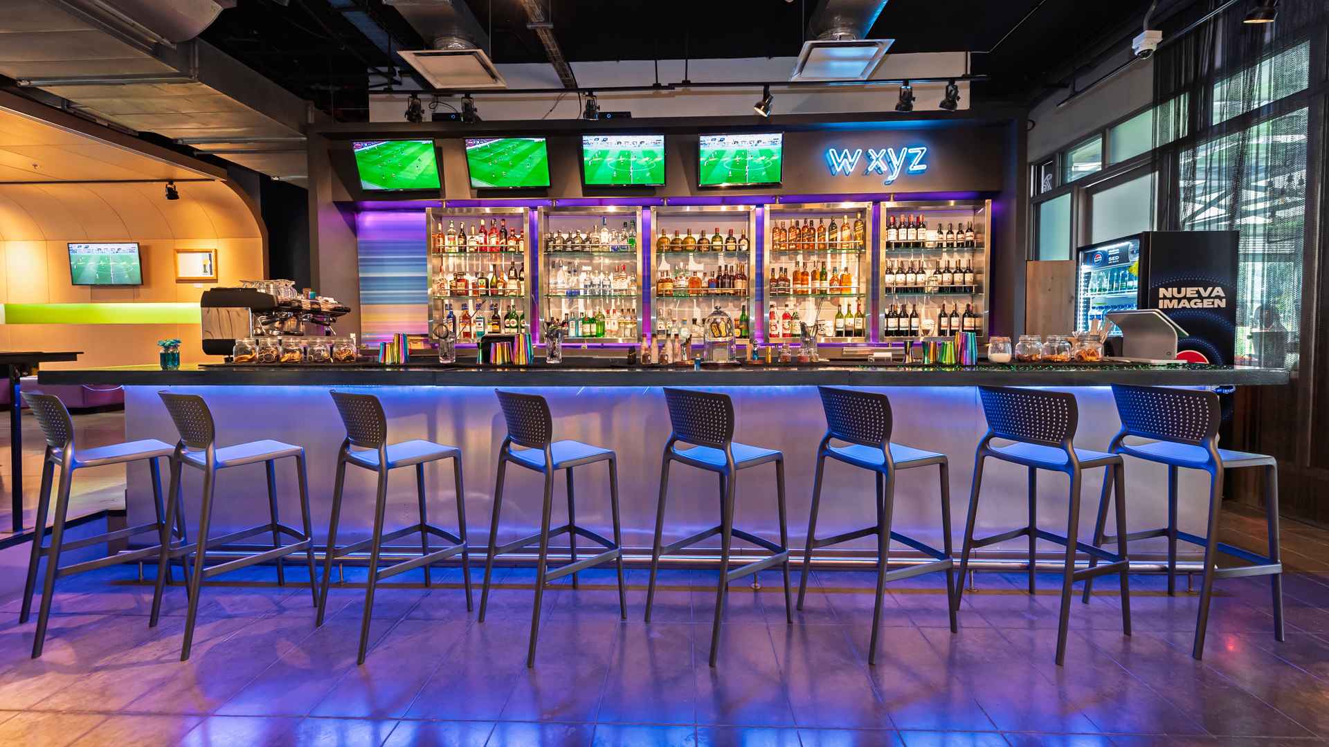 Un bar W XYZ vibrante y moderno con una barra iluminada, taburetes, pantallas de televisión y una gran variedad de bebidas.