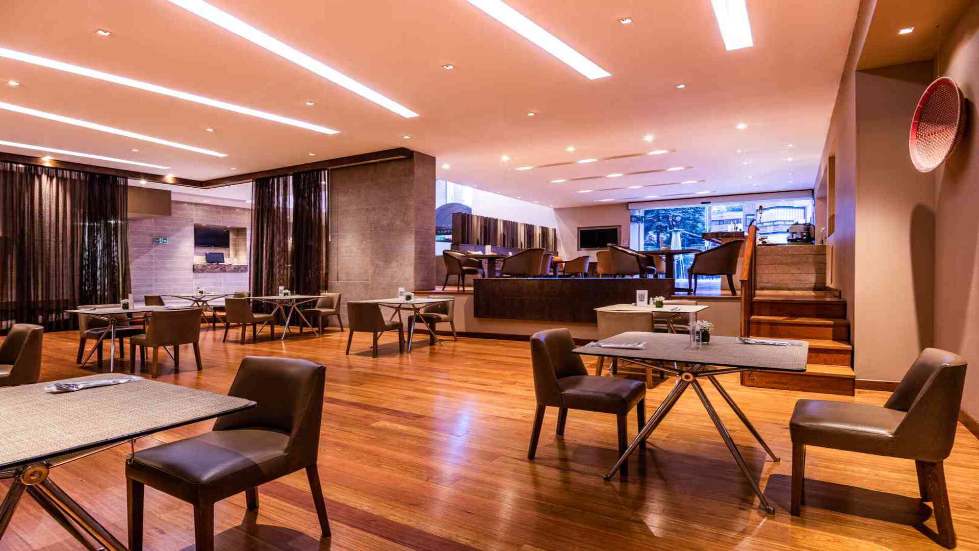 Un restaurante de hotel elegante con mesas y sillas de cuero, pisos de madera y una iluminación cálida que crea un ambiente acogedor.