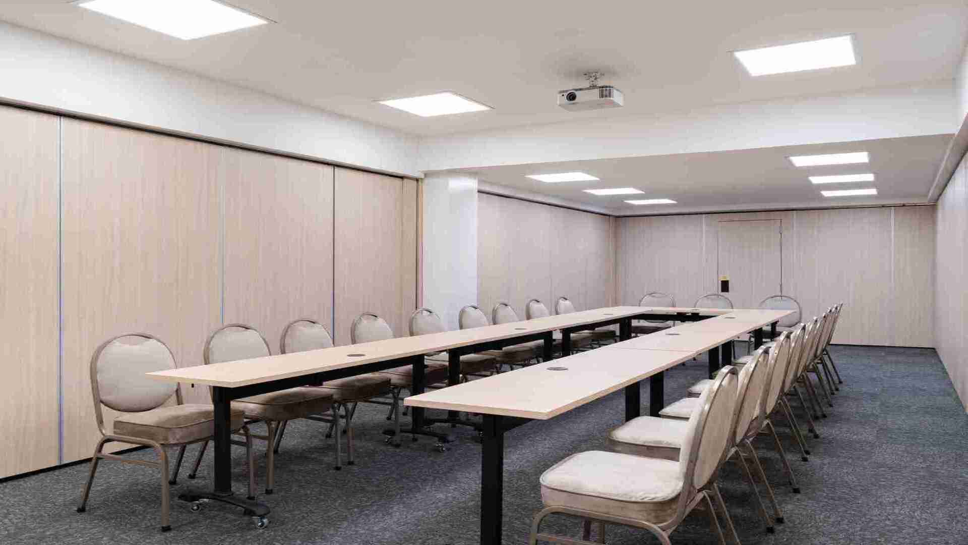 Una sala de reuniones dispuesta en forma de "U" con mesas y sillas cómodas, equipada con un proyector, ideal para conferencias y presentaciones.