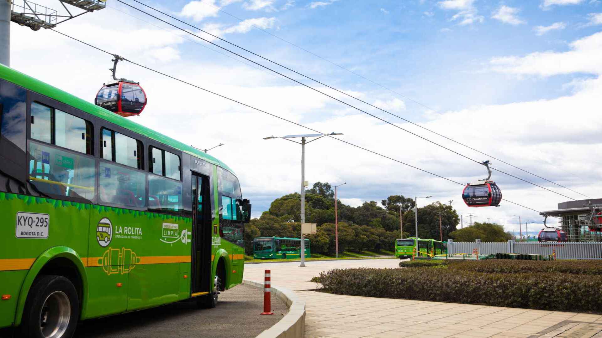 Buses de color verde y teleféricos rojos en una estación de transporte público en Bogotá bajo un cielo nublado. 