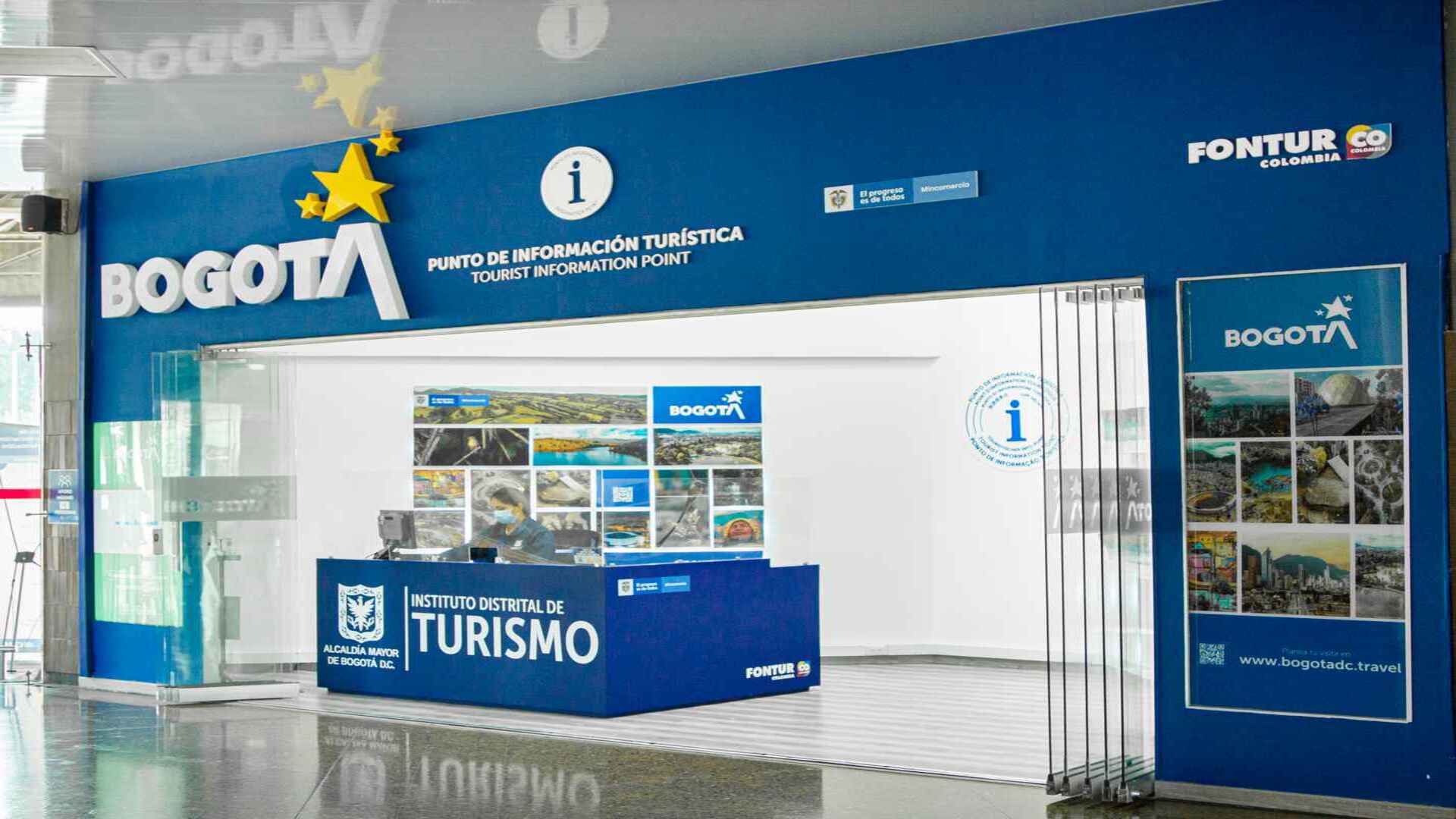 Entrada a un punto de información turística de Bogotá, con diseño moderno y un mostrador azul. 