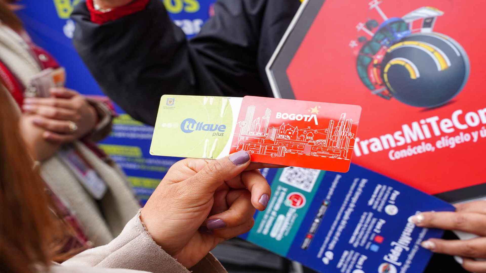 Una mano femenina sosteniendo dos tarjetas de transporte público de Bogotá, una verde y una roja. 