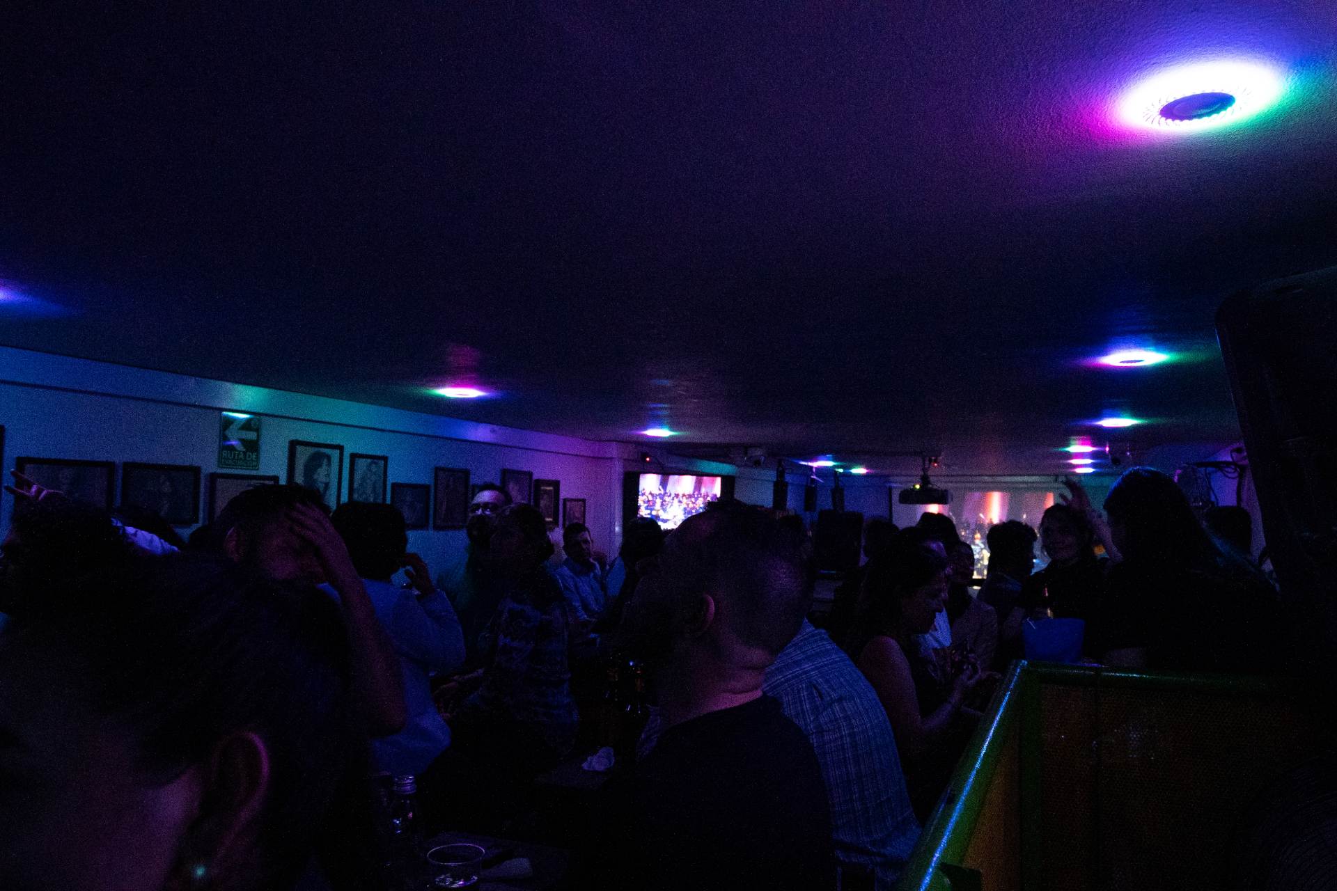 Interior El Perro y la Calandria en ambiente oscuro con grupo de personas bailando. Las paredes están adornadas con fotografías.