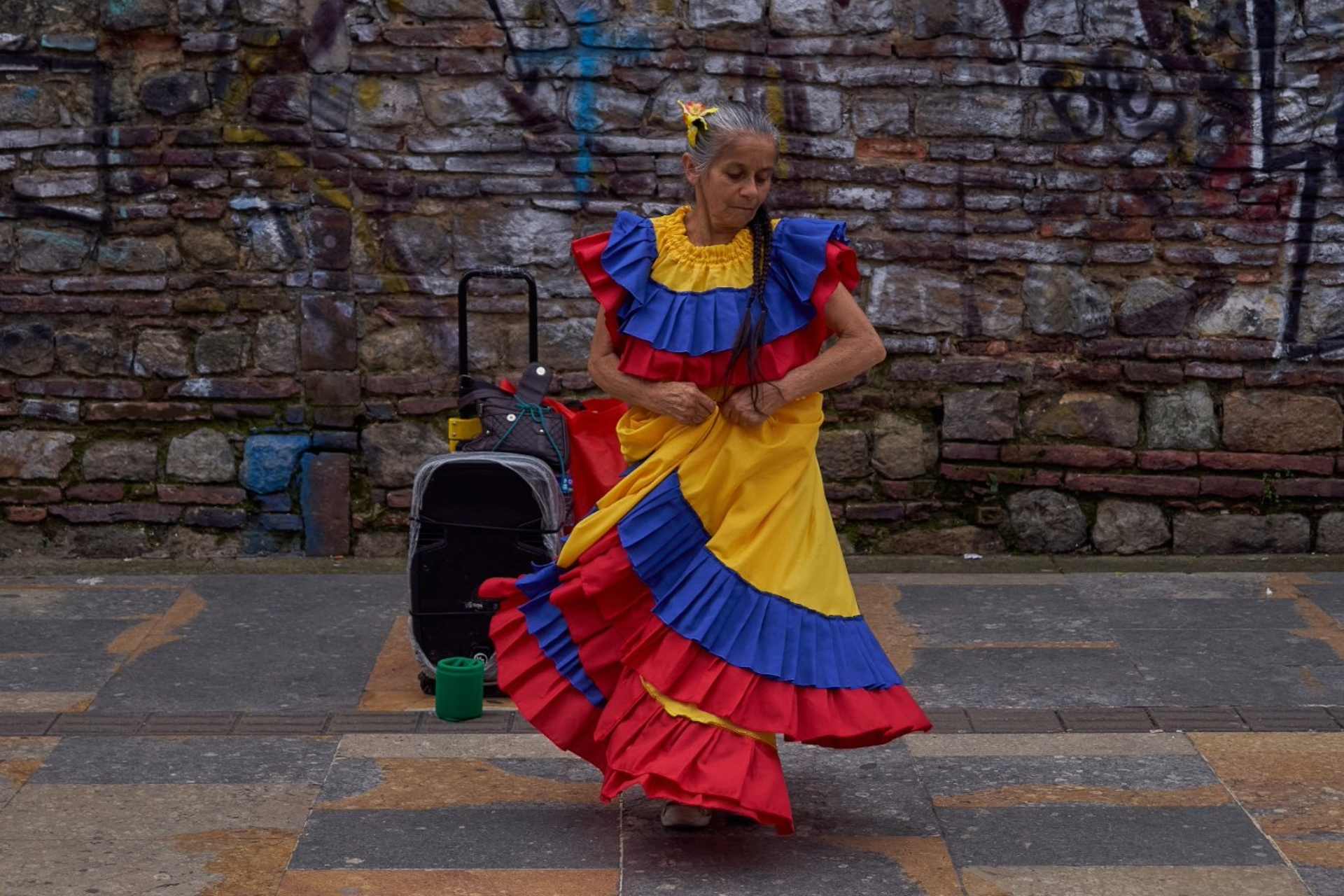Mujer anciana vestida con los colores de la bandera de Colombia baila en una calle con la música de una cabina de sonido.