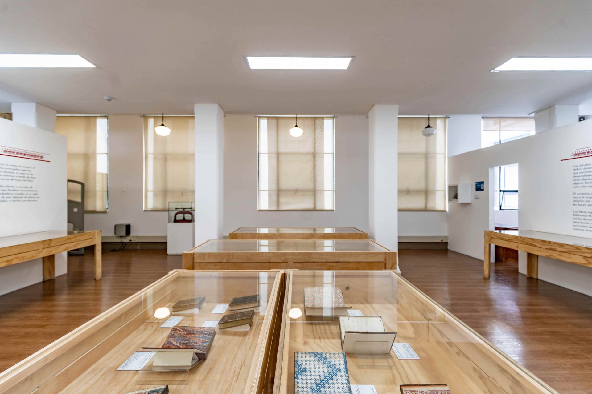 Biblioteca Nacional interior salon blanco iluminado con lámparas blancas con mesas y vitrinas con libros.