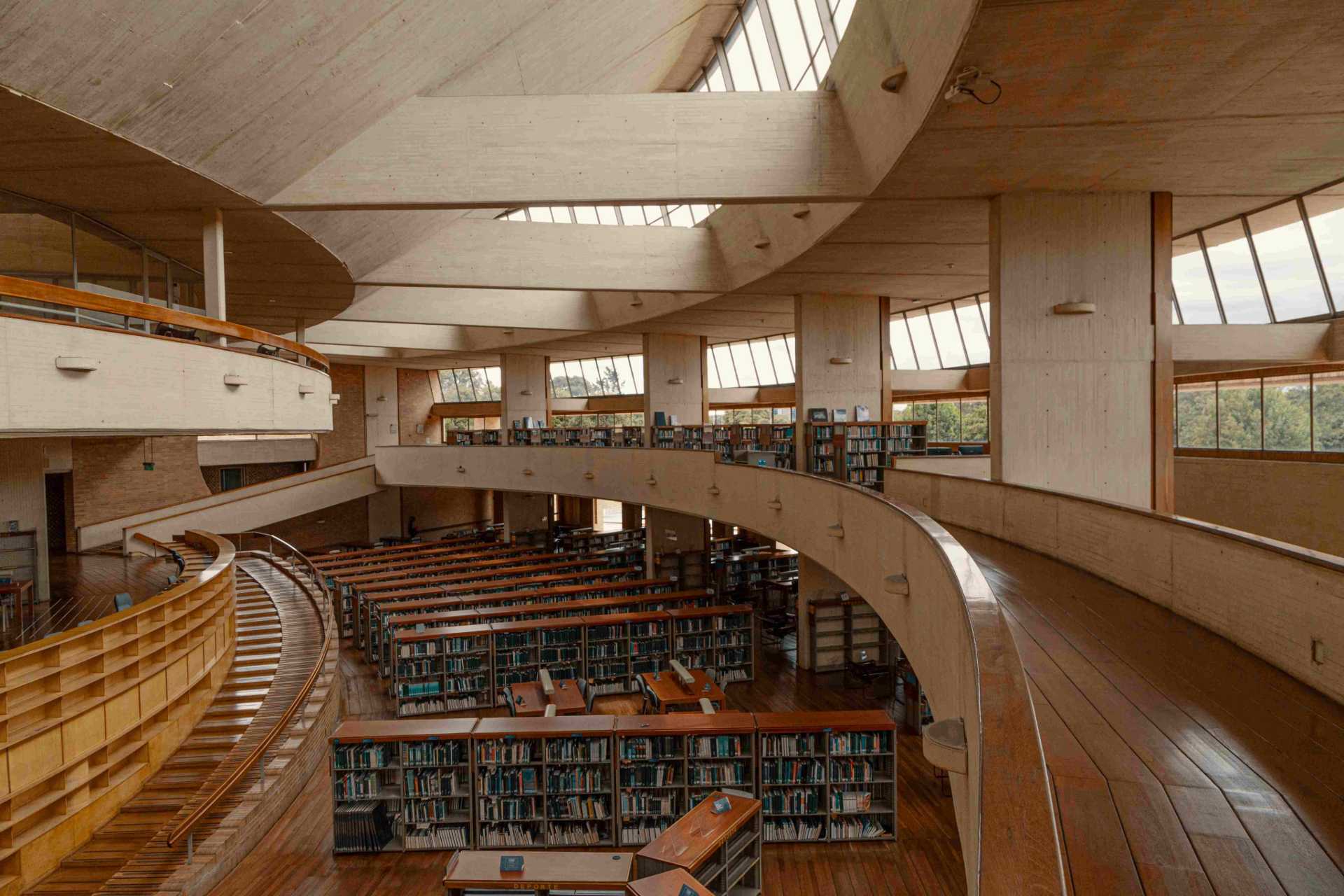 Biblioteca Virgilio interior en forma de espiral con paredes y pisos de madera, grandes ventanales y librerias repletas.