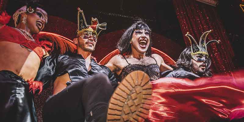 Grupo de 4 artistas de Chiquita bar disfrazados con trajes de arlequines y riendo.