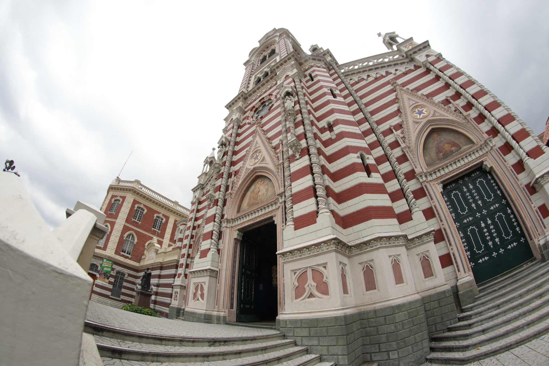 Iglesia Nuestra Señora Del Carmen fachada de día foto angular contrapicada de iglesia neogótica con rayas blancas y rojas. Dos puertas de madera negra, una abierta y otra cerrada.