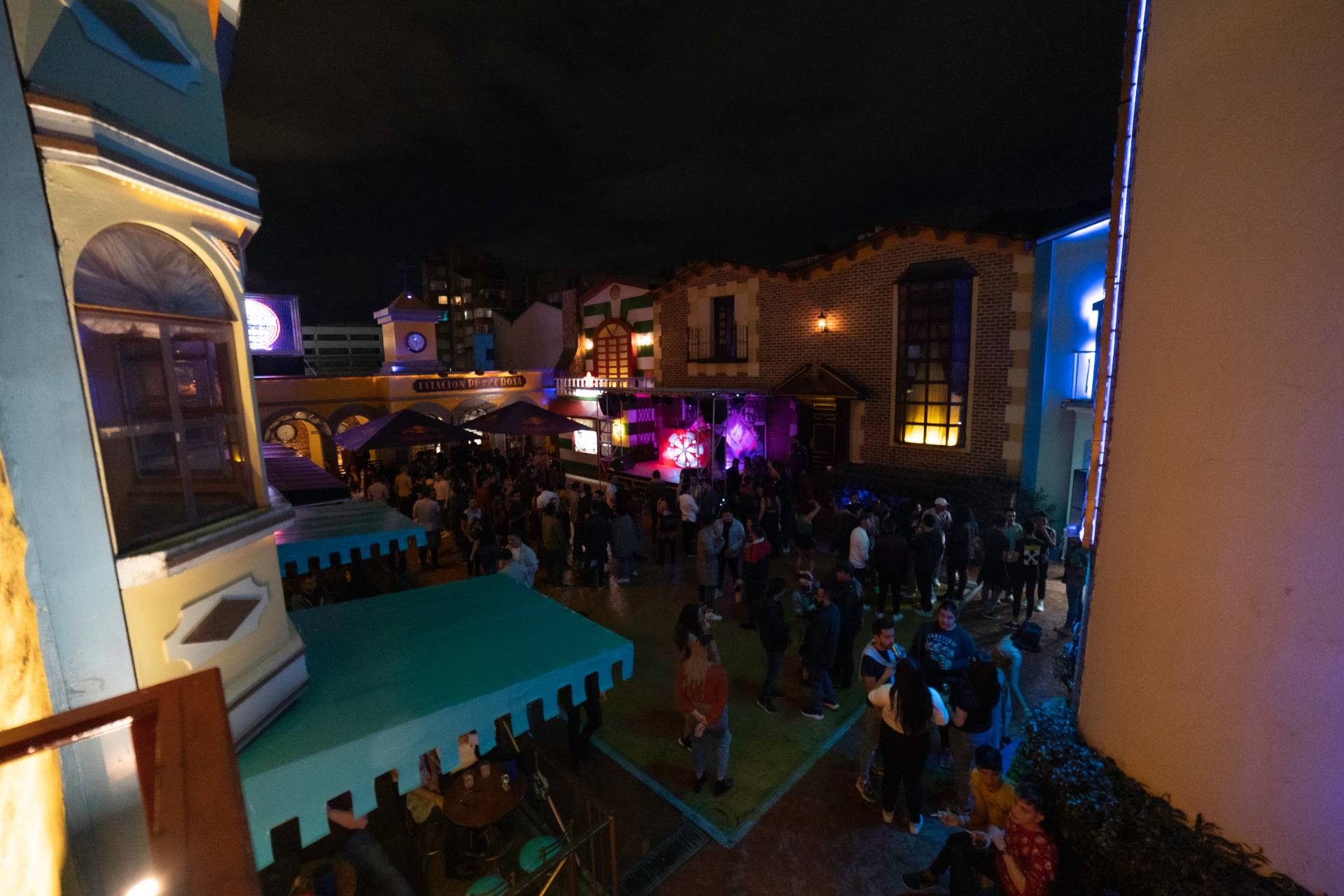 Theatron en plazoleta interior de noche con fachada de castillos y personas bailando alrededor.